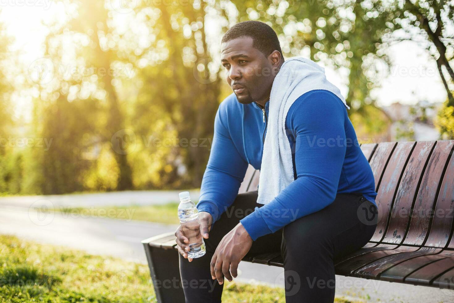 Exhausted man after exercise drinking water while sitting on bench. photo