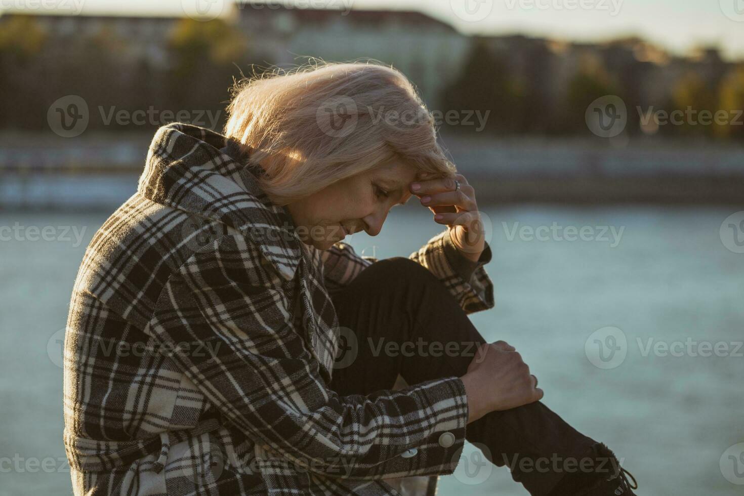 Sad senior woman sitting by the river alone.Toned image. photo