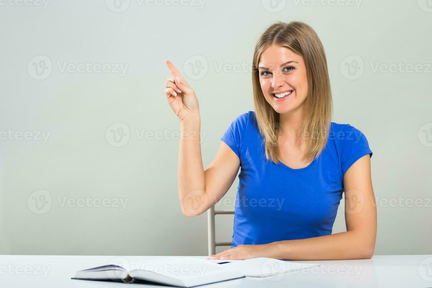 Beautiful female student sitting at the table and pointing. photo