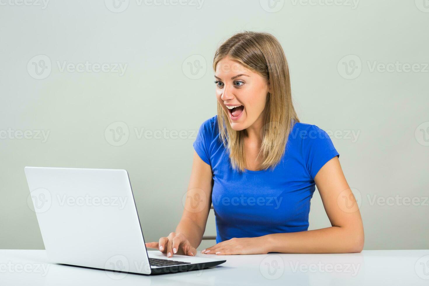 Excited young woman sitting at the table and using laptop. photo