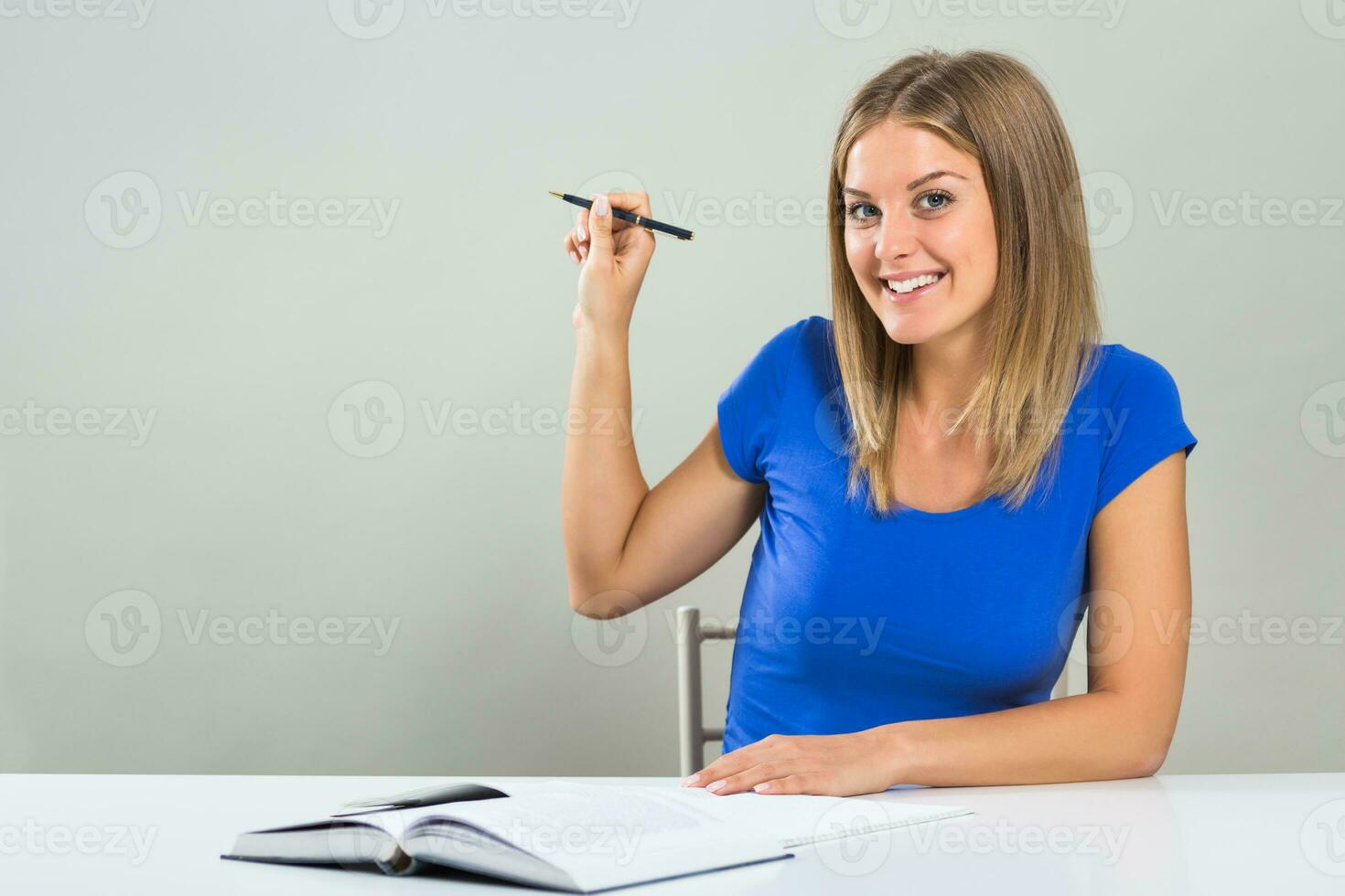 Beautiful female student sitting at the table and pointing with pen. photo