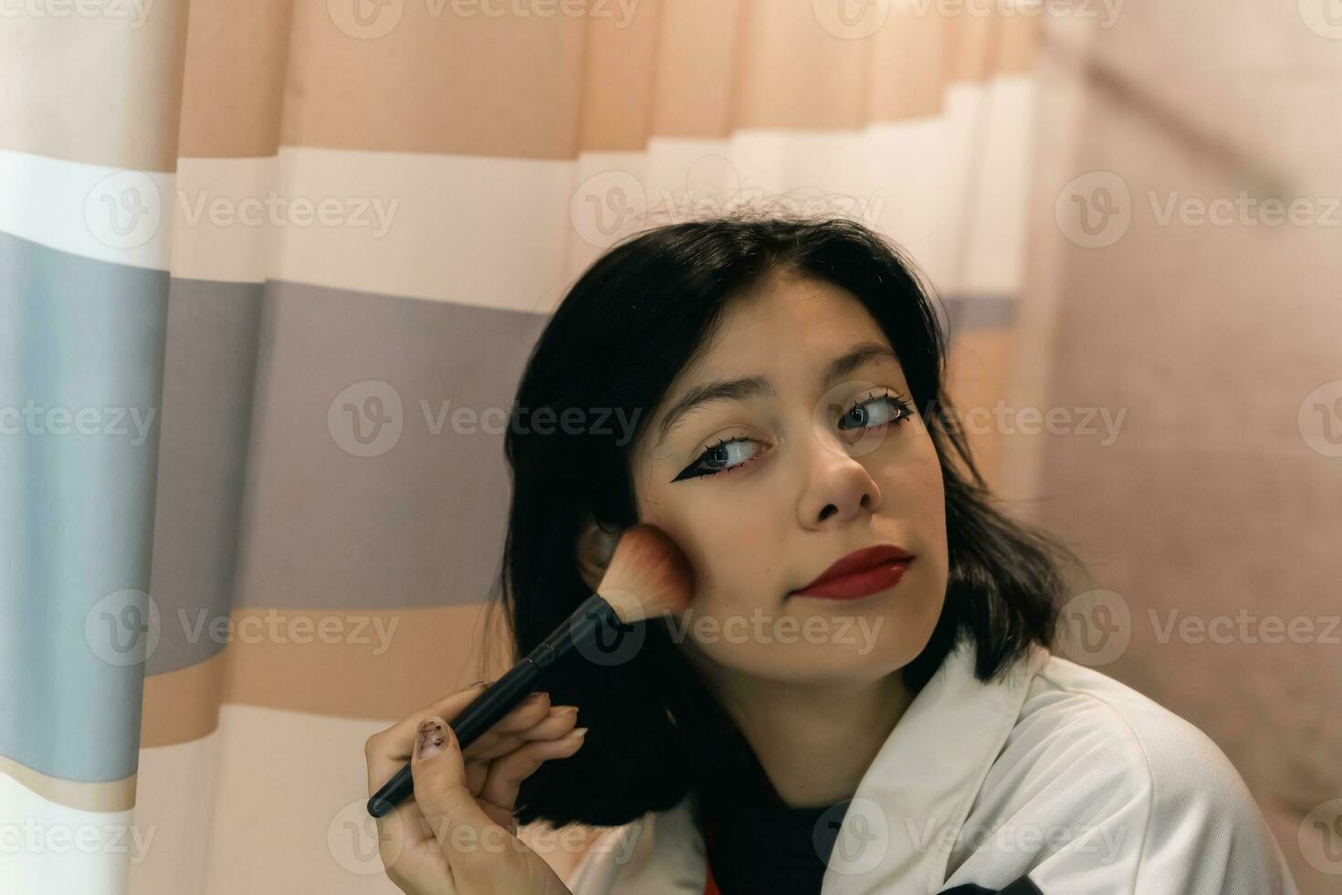 retrato de Adolescente niña contorneado con maquillaje cepillo en frente de espejo foto