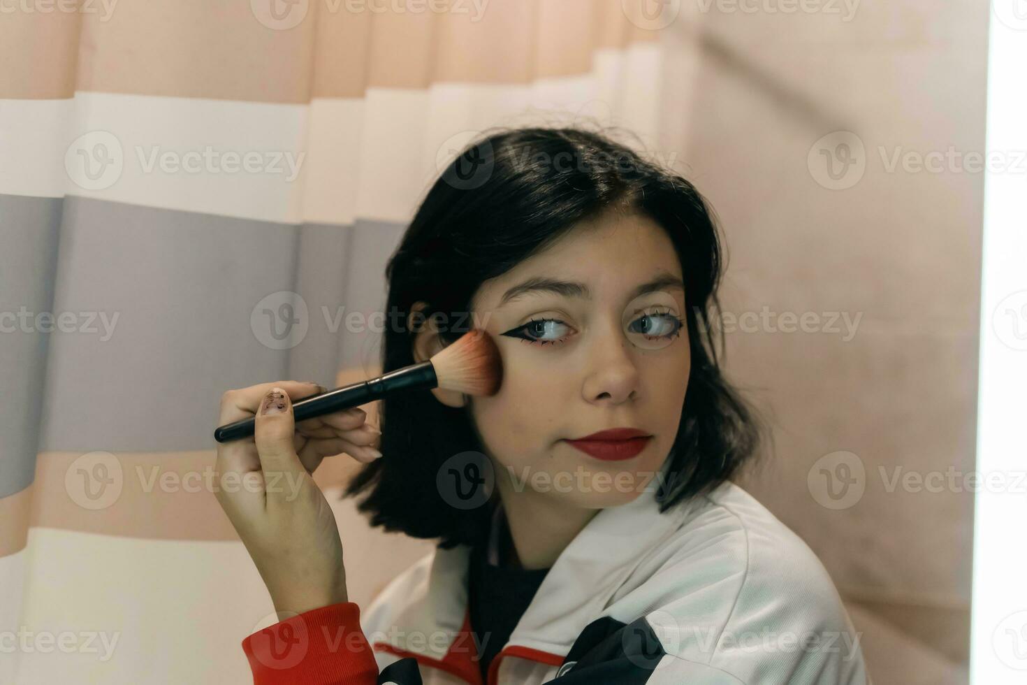 Adolescente niña aplicando maquillaje con un suave cepillo en frente de el espejo foto