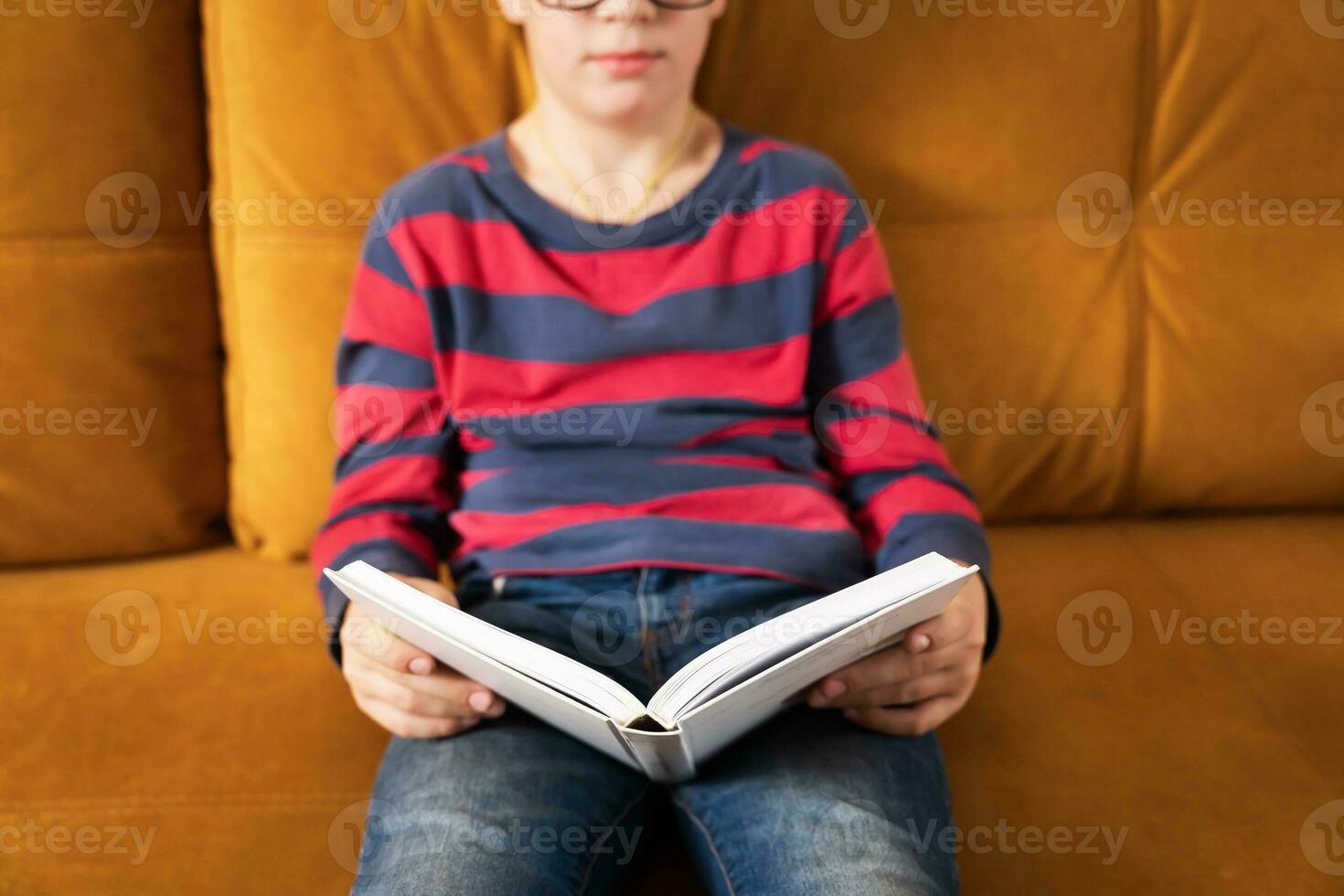 Young Curious Boy with Glasses Delving into a Book on the Couch photo
