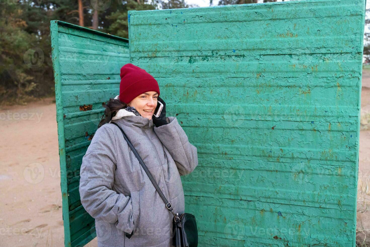 Autumn Fashion. Woman in Cozy Outfit Using Phone Inside Vintage Beach Changing Booth photo