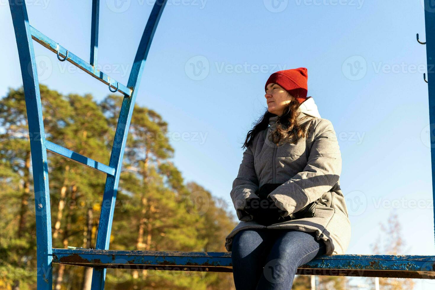 woman in an autumn jacket and hat is sitting alone on a bench on a deserted autumn beach on a sunny day photo