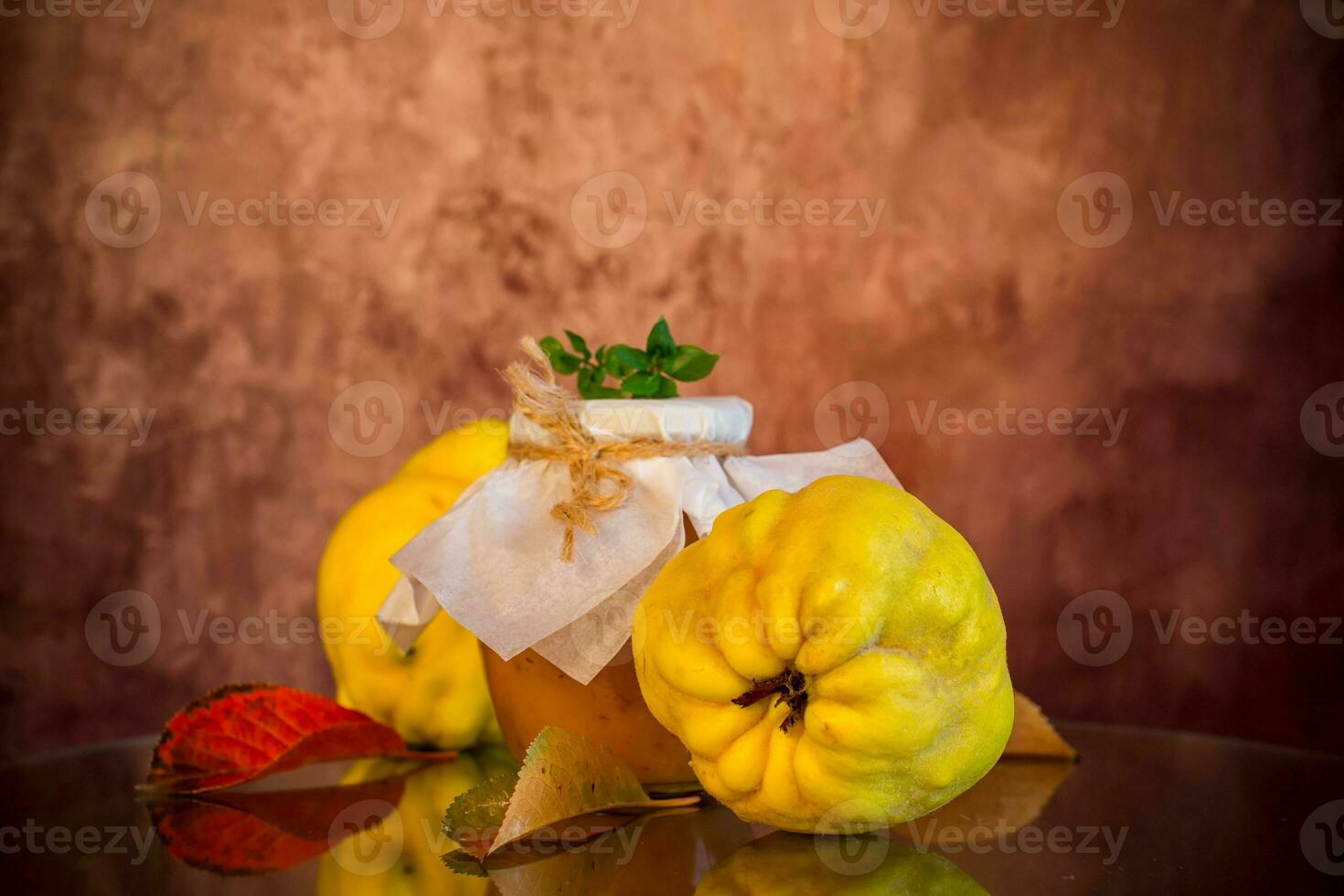 Ripe quince fruits with jam in a glass jar on a dark wooden table. photo