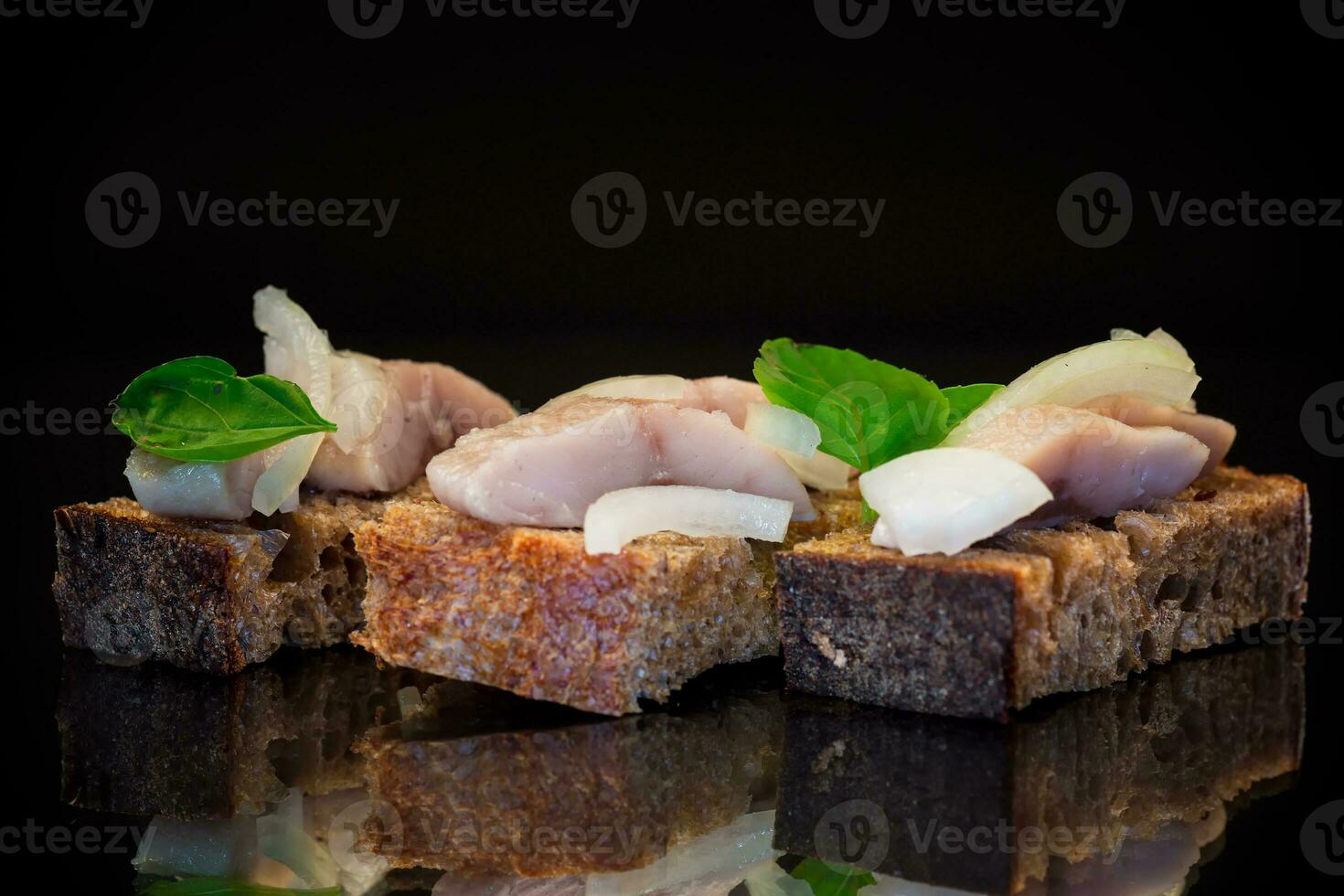canape of pieces of salted herring with onions on a fresh dark piece of bread. photo