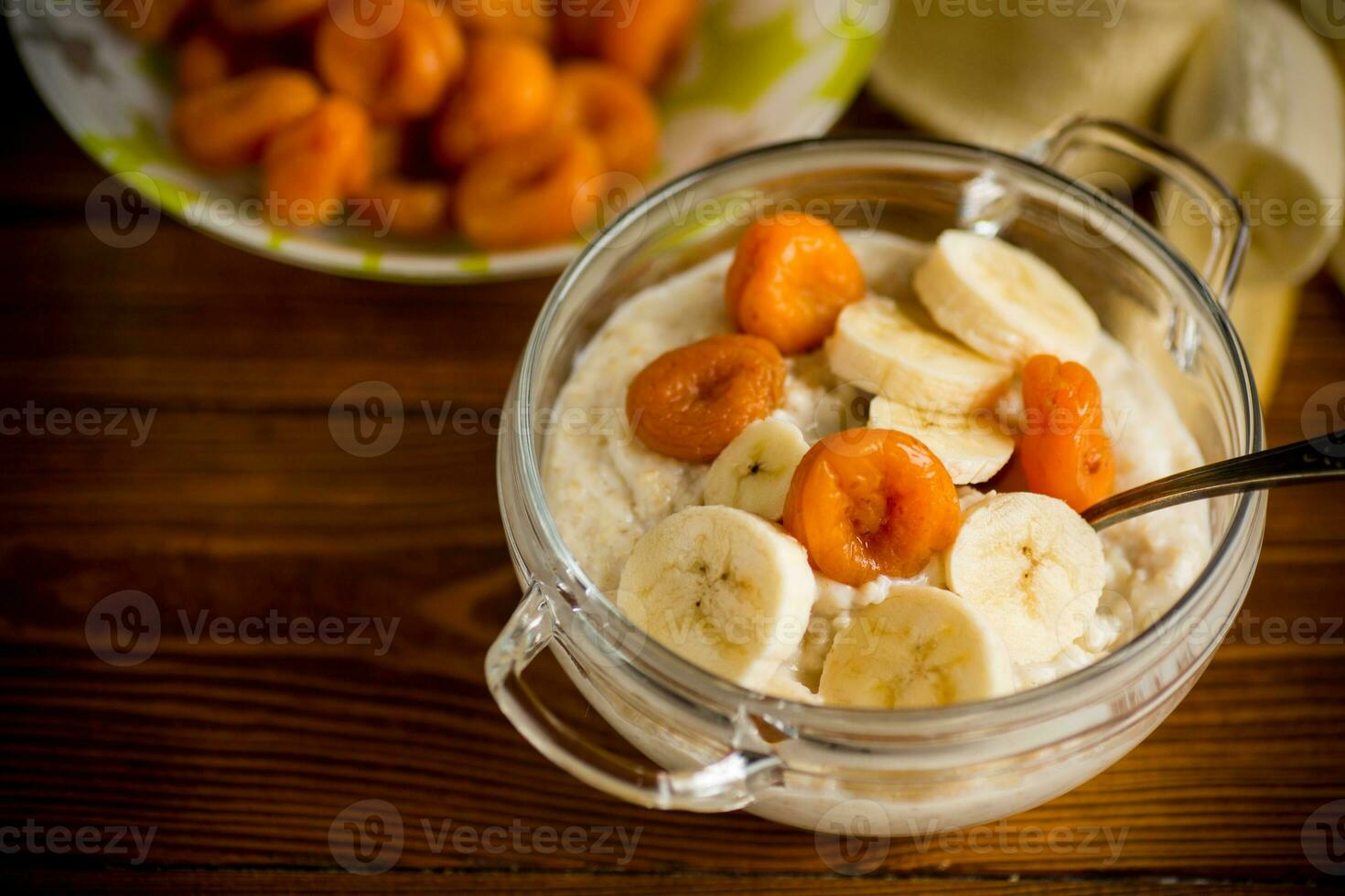 cooked boiled sweet oatmeal with with dried apricots and bananas in a bowl photo