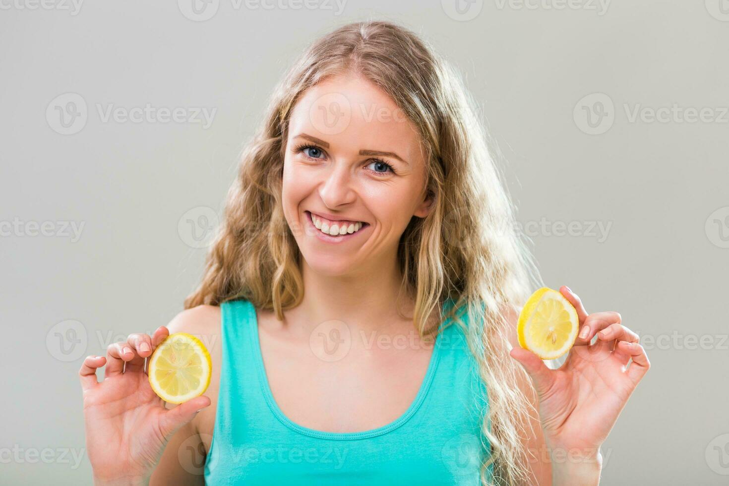 Beautiful young woman showing slices of lemon on gray background photo