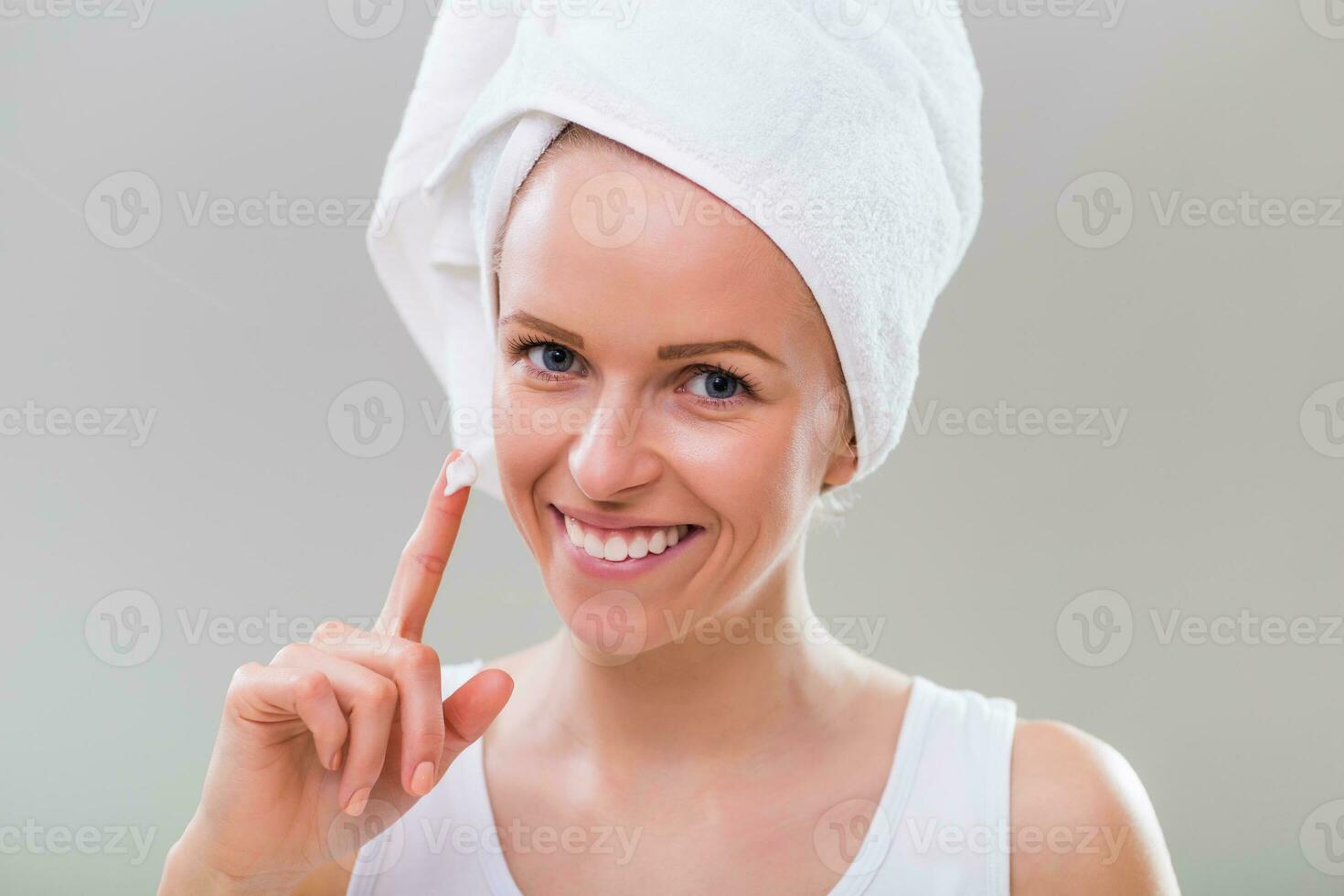 Beautiful young woman showing moisturizer, on gray background. photo