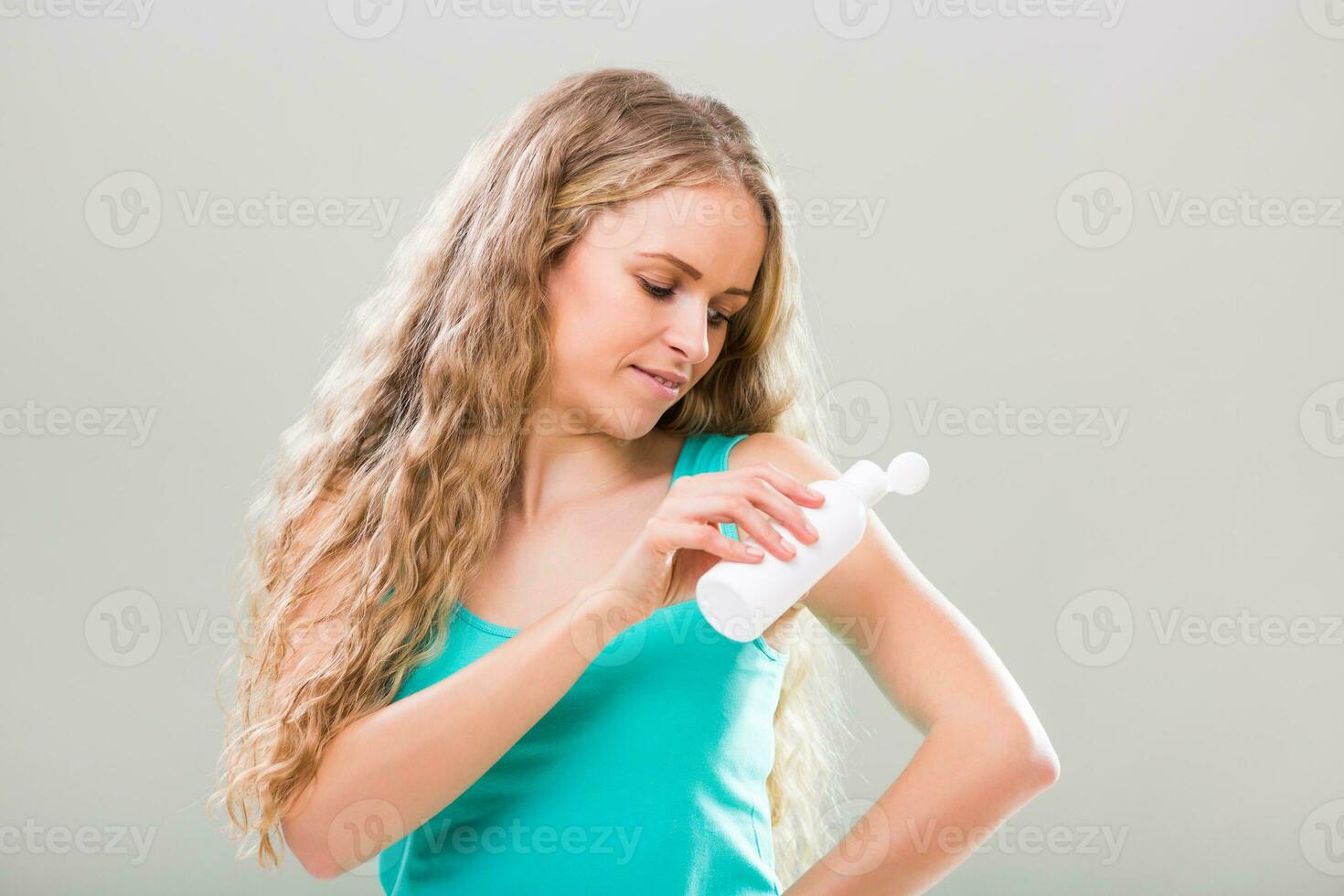 Beautiful young woman applying lotion on her arm on gray background. photo
