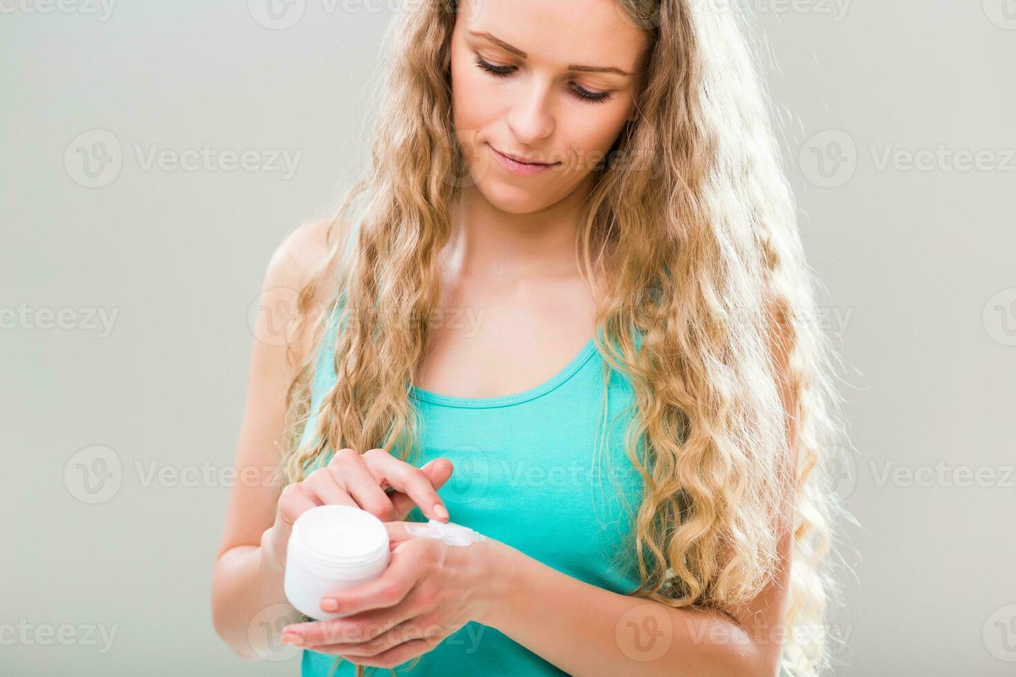 Beautiful young woman applying hand cream on gray background. photo