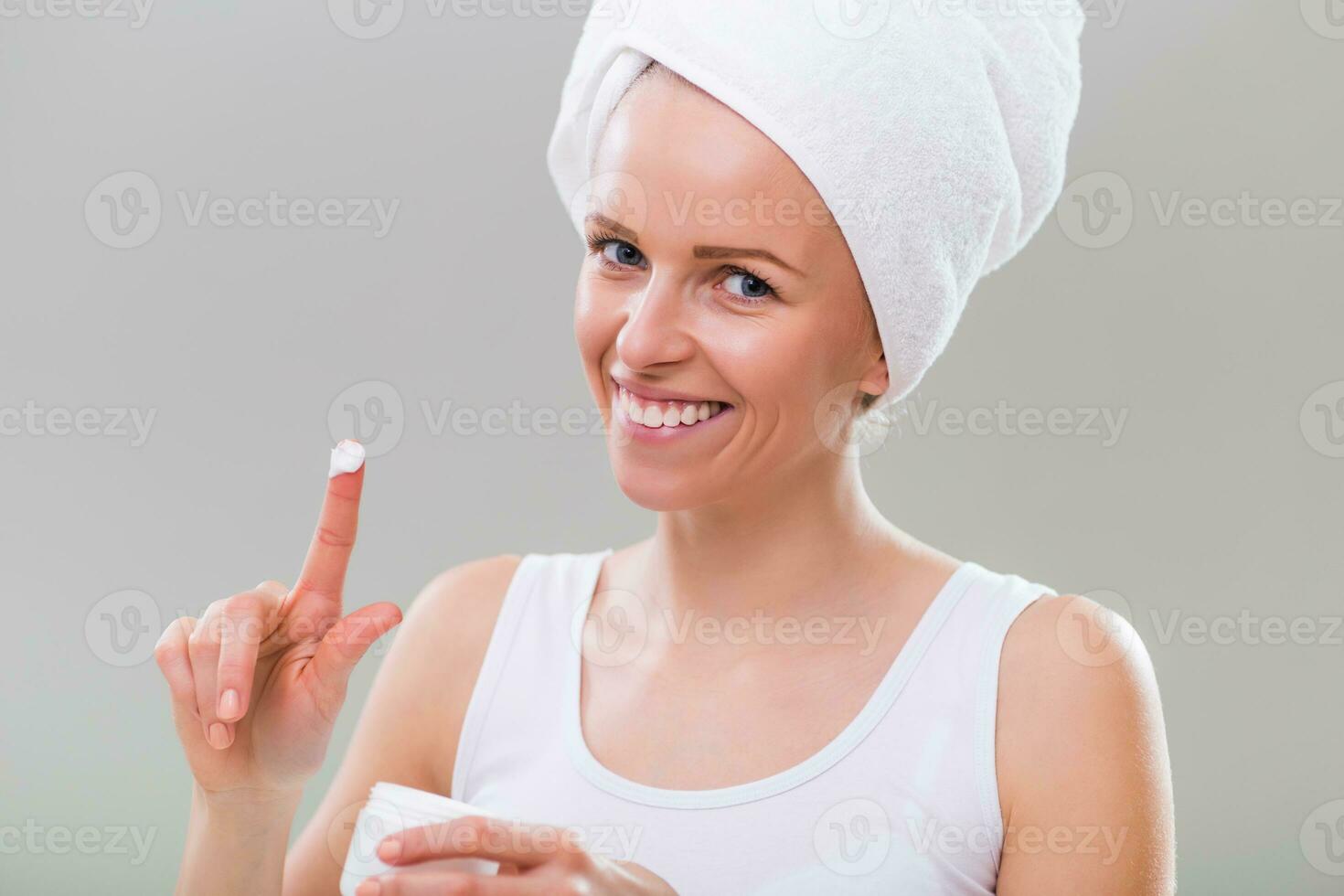 Beautiful young woman showing moisturizer, on gray background. photo