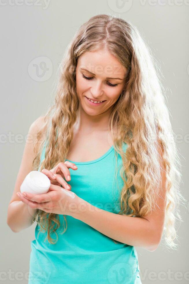 Beautiful young woman applying hand cream on gray background. photo