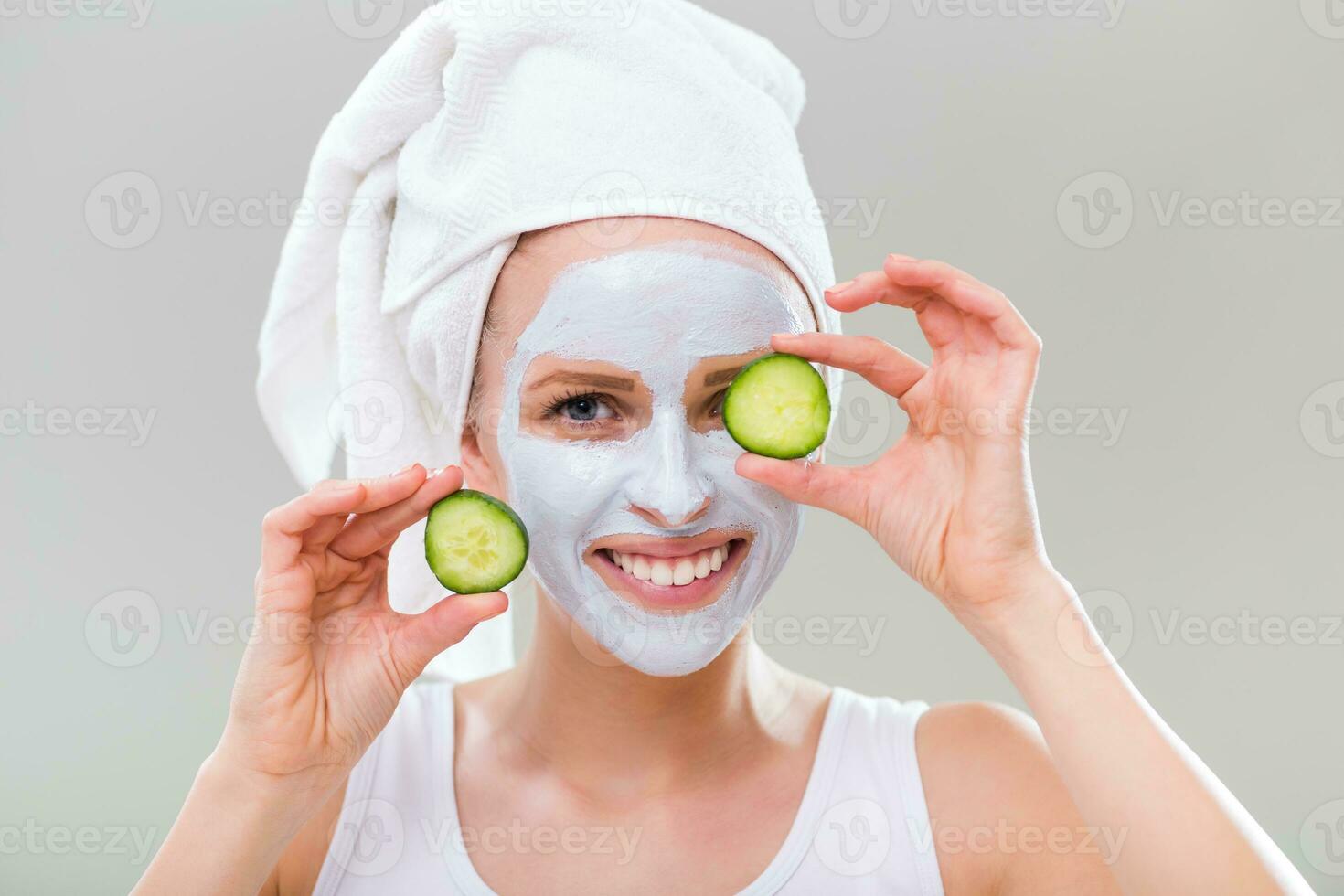 Young woman with facial mask holding slices of cucumber on gray background. photo
