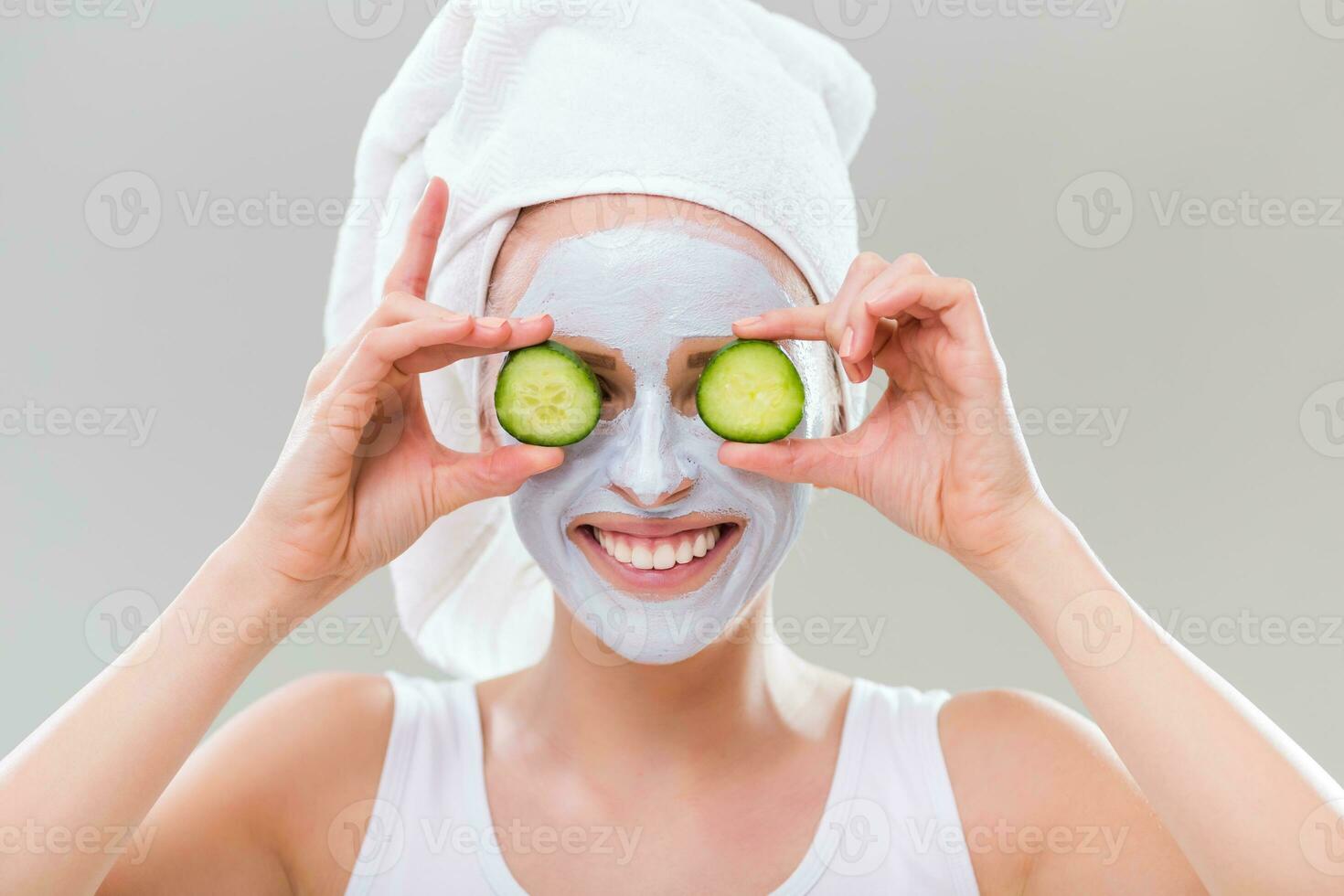 Young woman with facial mask holding slices of cucumber on gray background. photo