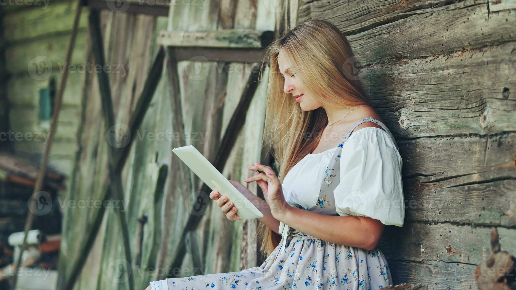 Village Slavic girl flipping a tablet in the countryside by the barn. photo