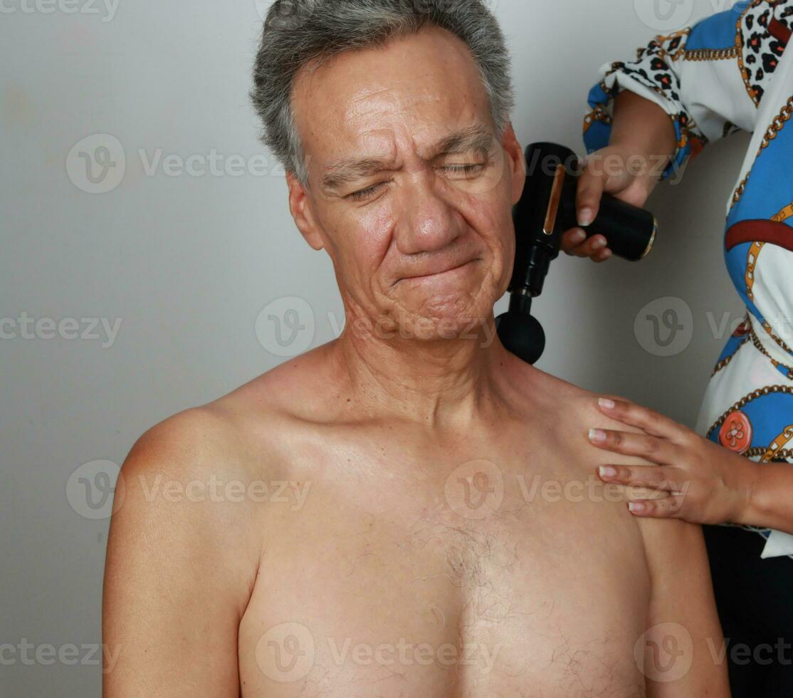 Older Mature Man having a massage on his upper back and neck for pain relief with a Percussion Massage Gun photo