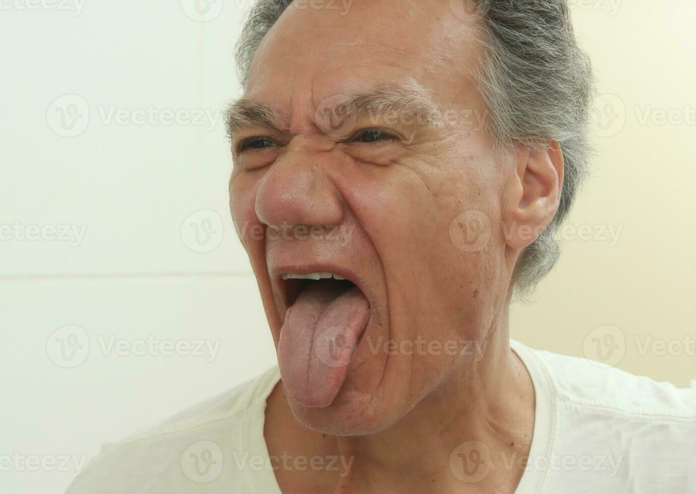 Older Mature man sticking his tongue out examining it in front of a mirror photo