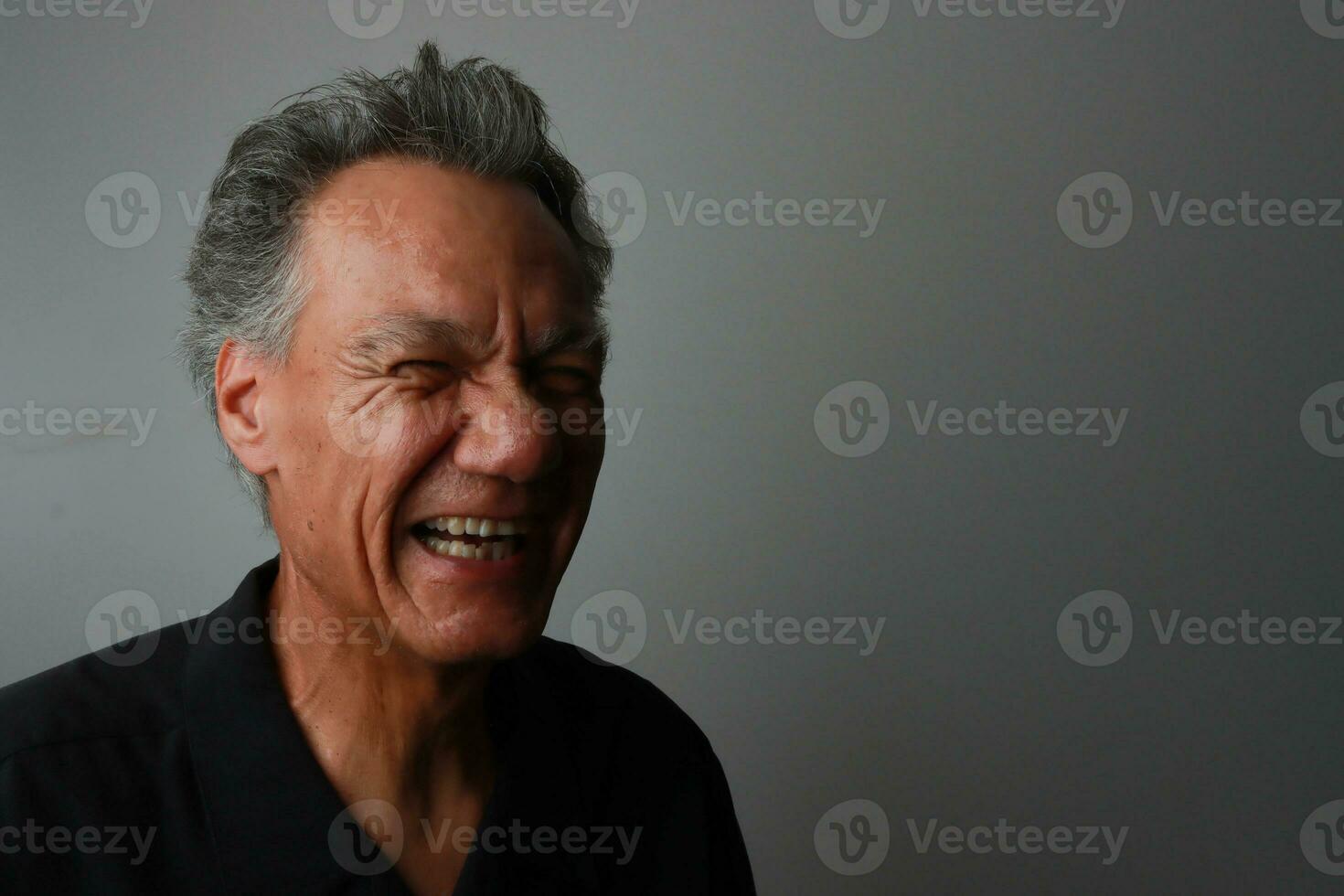 Older Mature Man against a Gray background breaking out in laughter photo