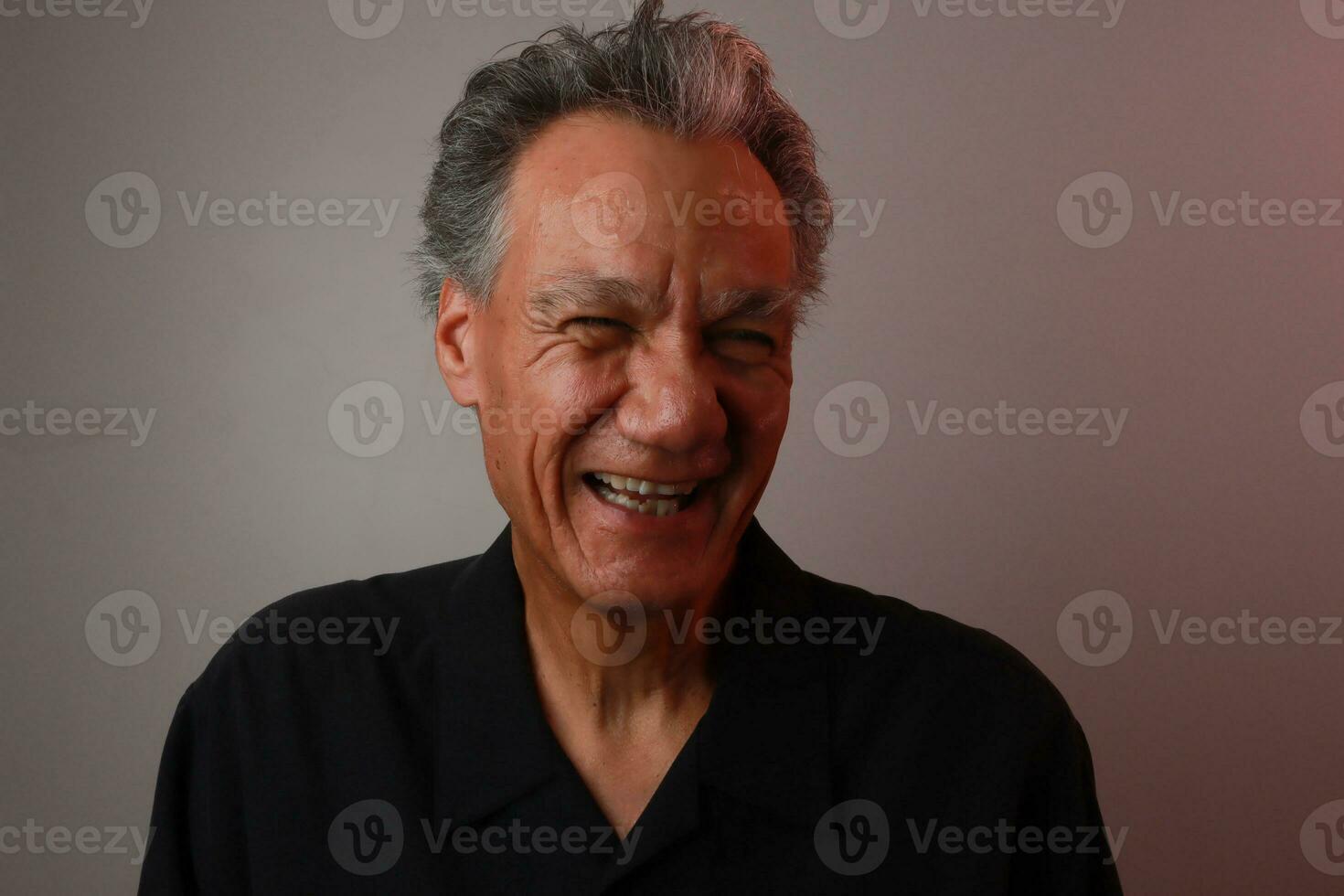 Older Mature Man against a Gray background breaking out in laughter photo