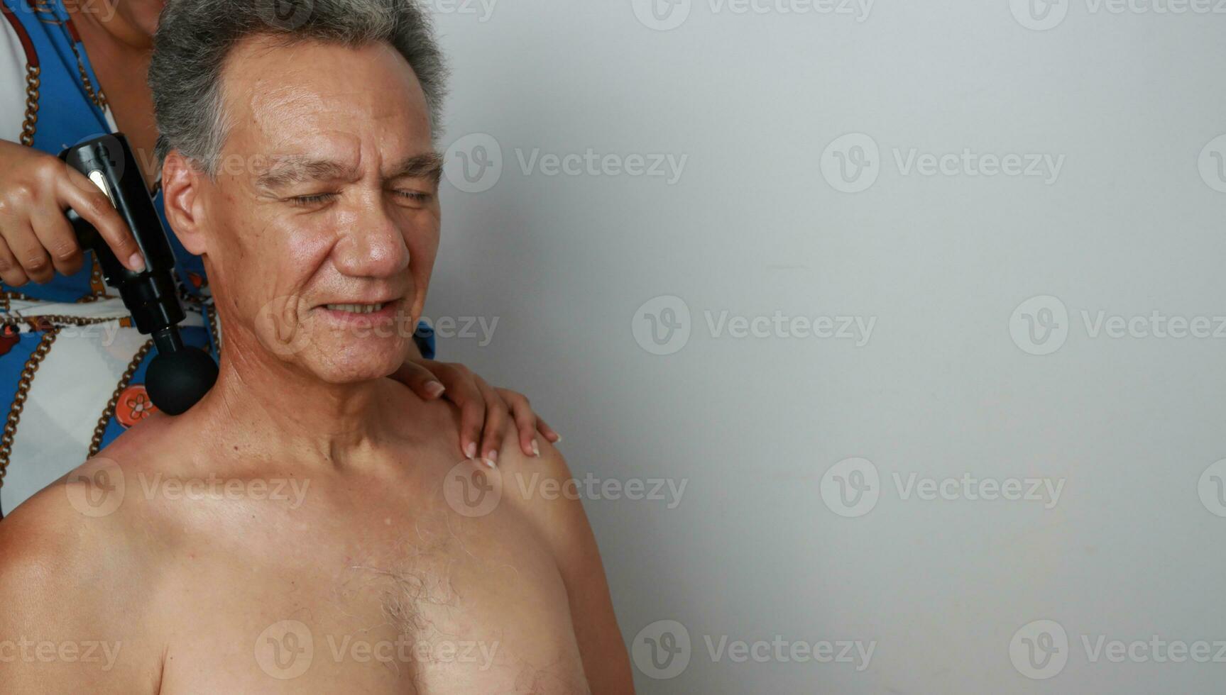 Older Mature Man having a massage on his upper back and neck for pain relief with a Percussion Massage Gun photo