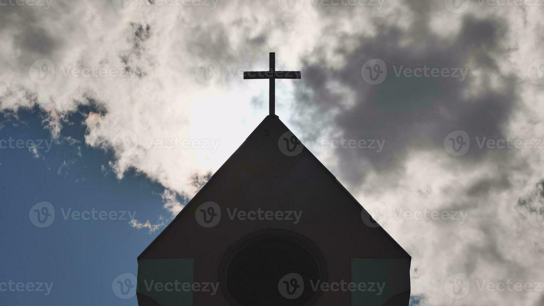 The silhouette of a Catholic church tower against a background of sun and clouds. photo