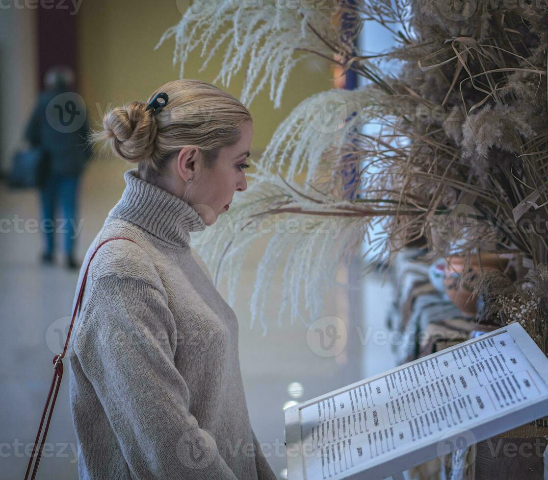 A blonde girl in a warm sweater looks at the menu at the entrance to a cafe photo