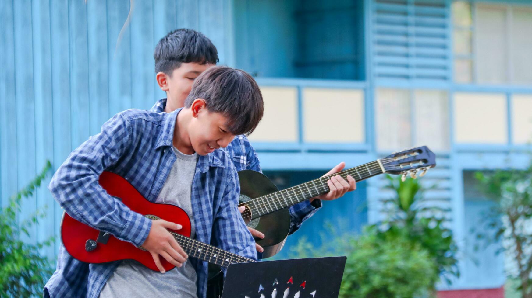 Young Asian boys are playing acoustic guitars in front of a house concept of learning and free time activities photo