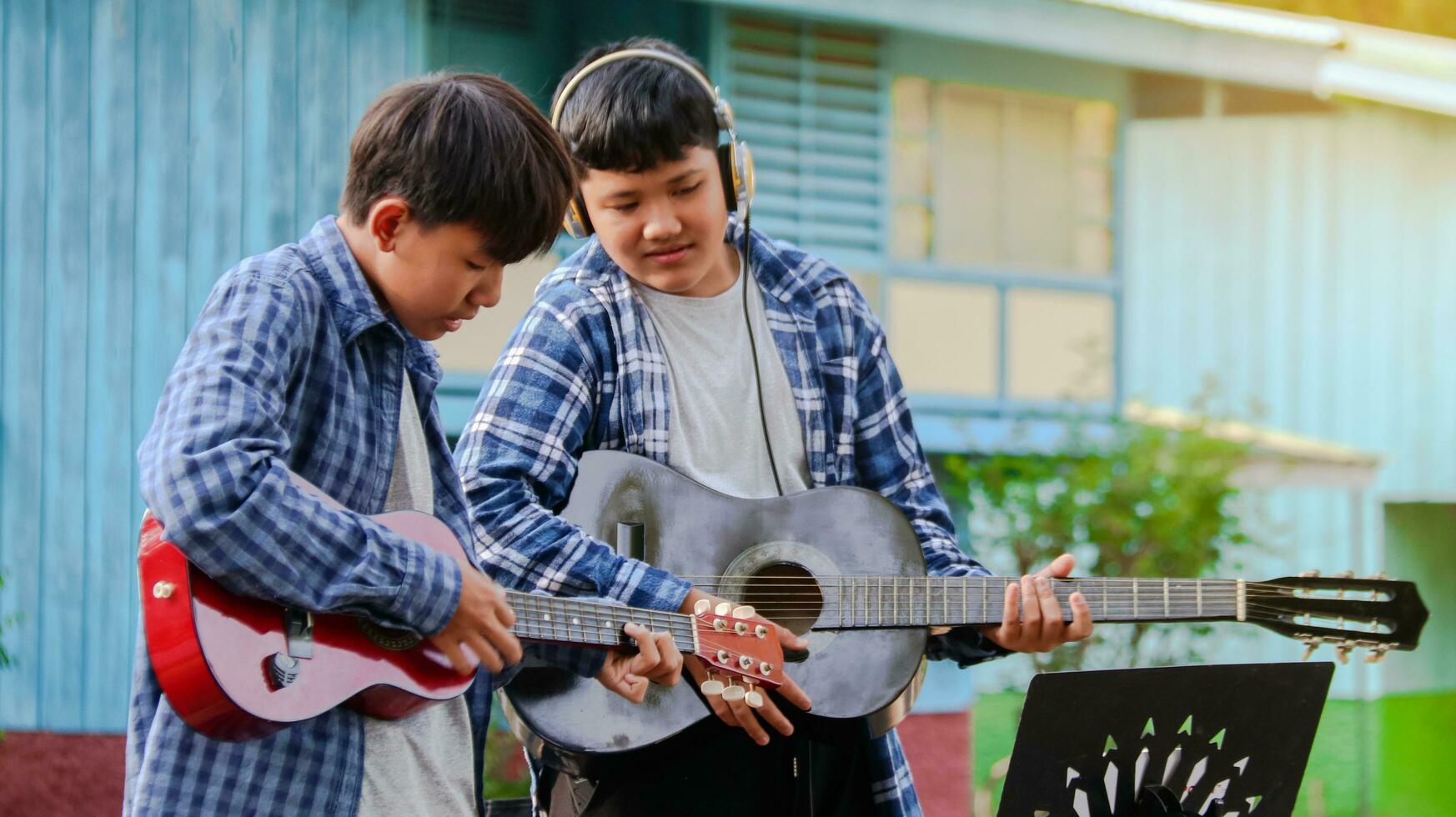 joven asiático Niños son jugando acústico guitarras en frente de un casa concepto de aprendizaje y gratis hora ocupaciones foto