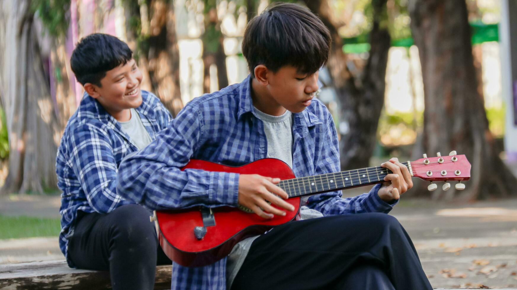 Young Asian boys are playing acoustic guitars in front of a house, soft and selective focus photo