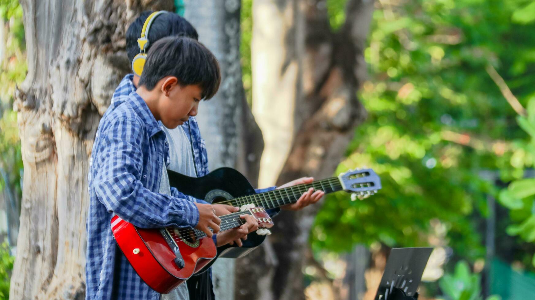 joven asiático Niños son jugando acústico guitarras en frente de un casa concepto de aprendizaje y gratis hora ocupaciones foto