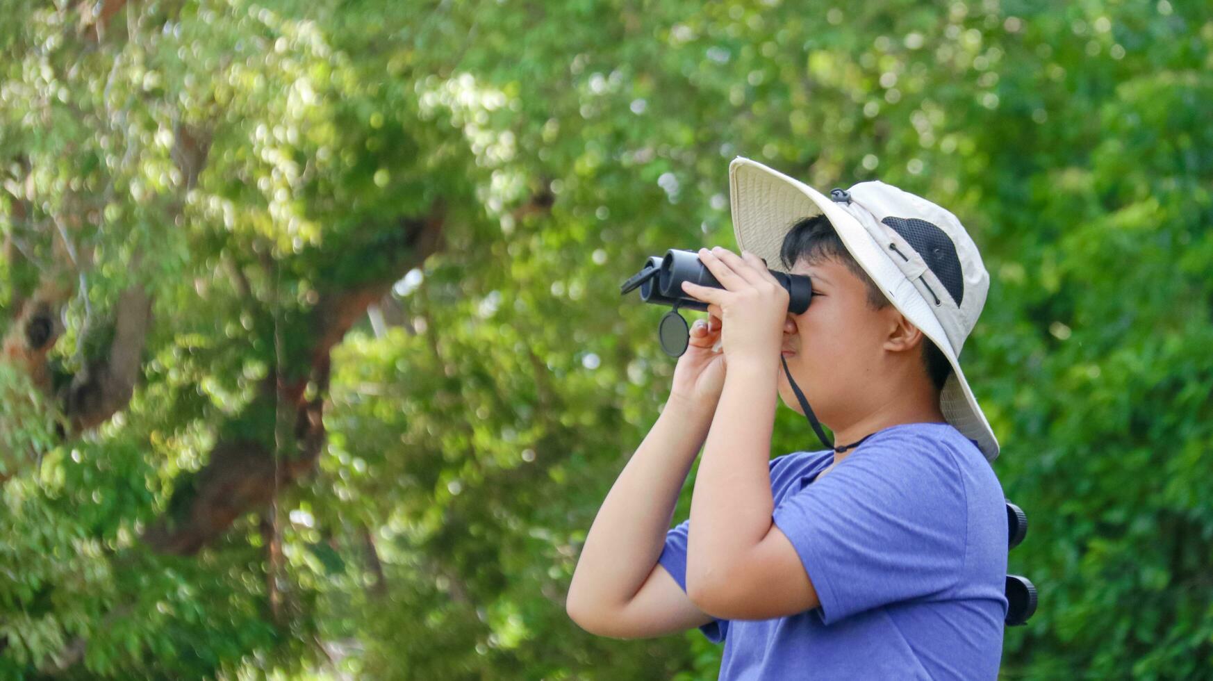 Young Asian boys are using a binocular to lookout for birds and animals in a local park, soft and selective focus photo