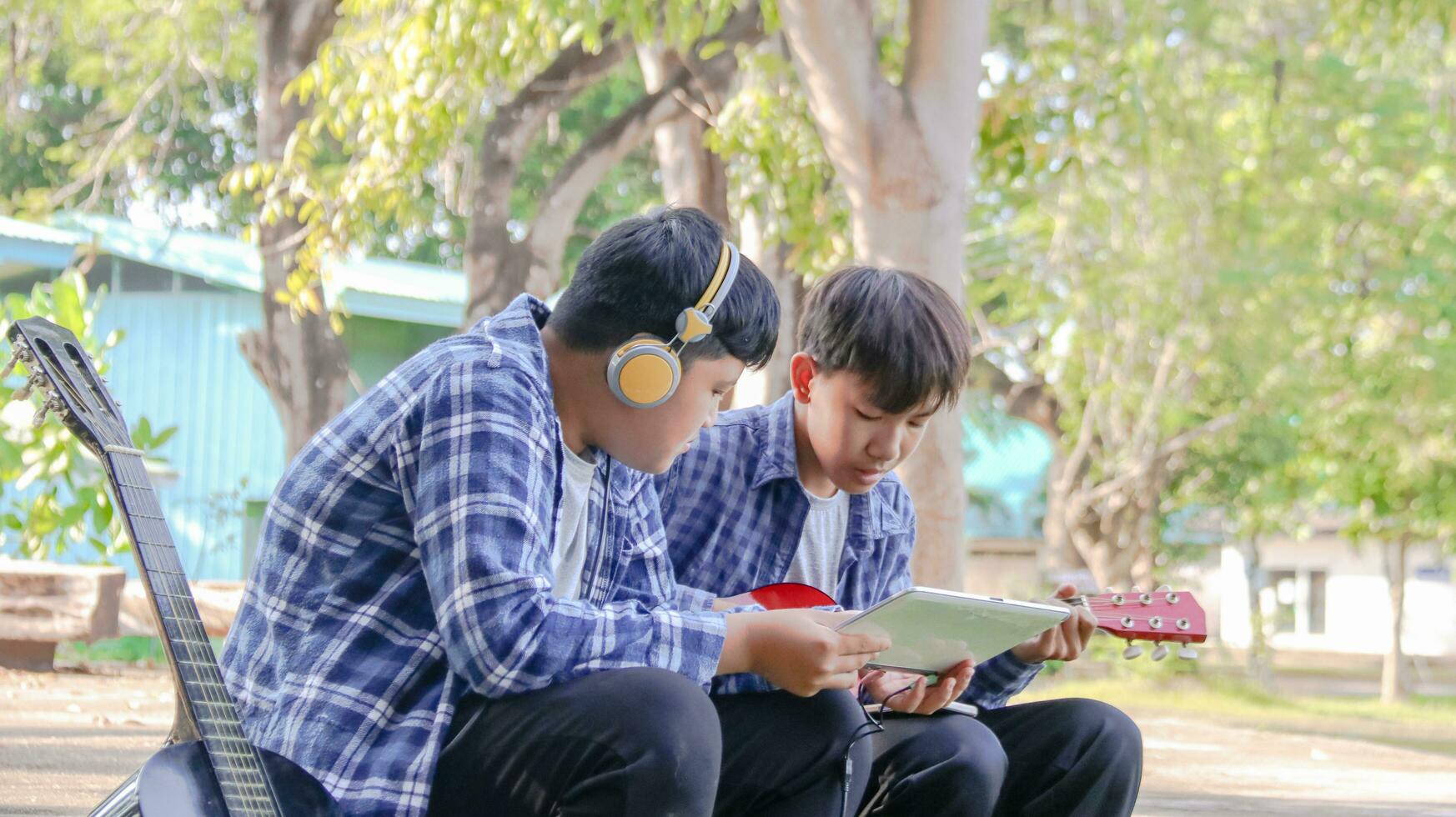 Young Asian boys are playing acoustic guitars in front of a house, soft and selective focus photo