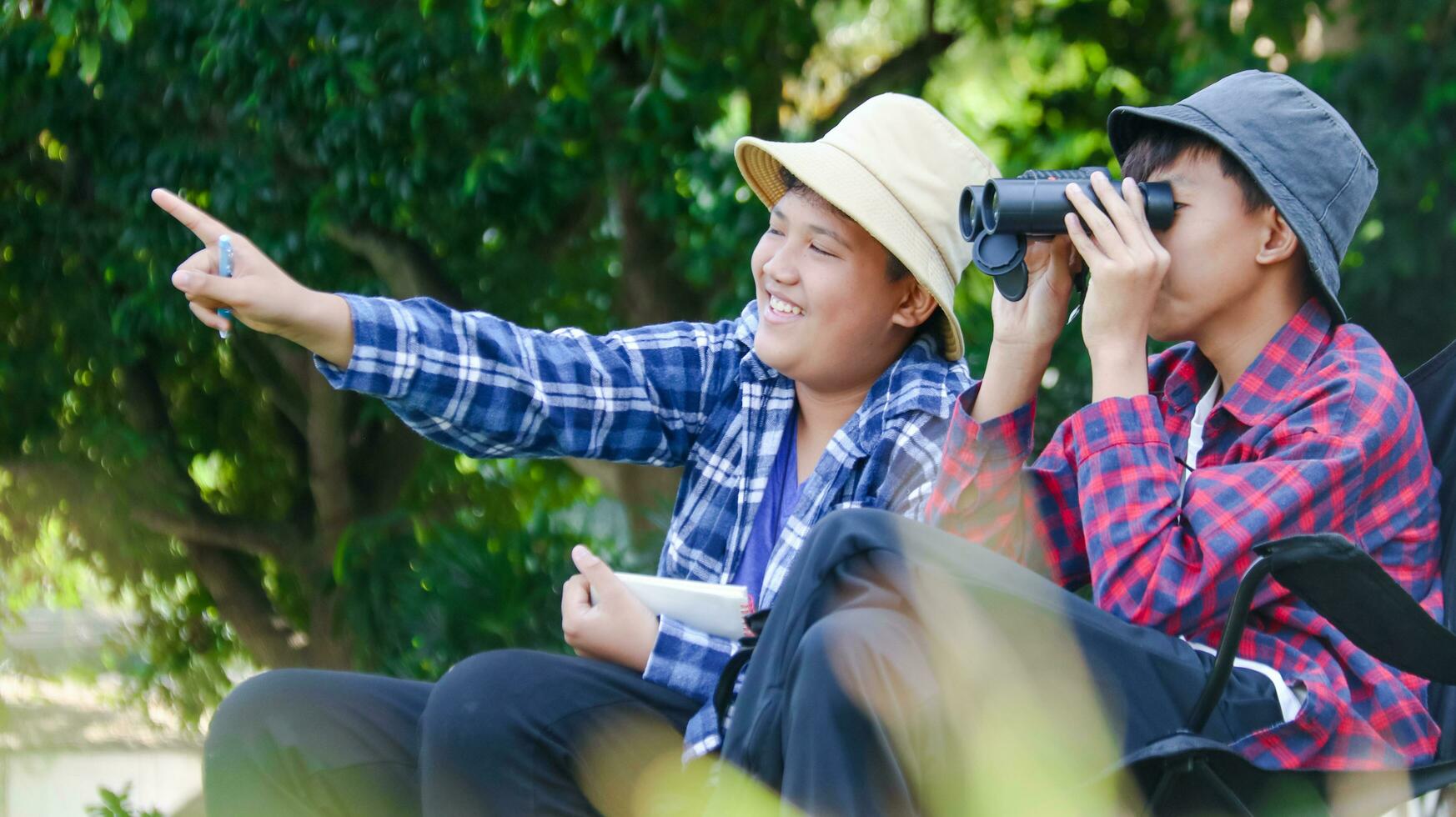 Young Asian boys are using a binocular to lookout for birds and animals in a local park, soft and selective focus photo