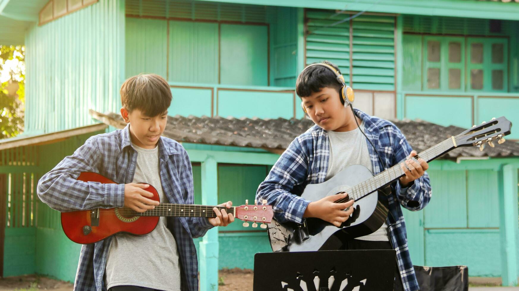Young Asian boys are playing acoustic guitars in front of a house, soft and selective focus photo