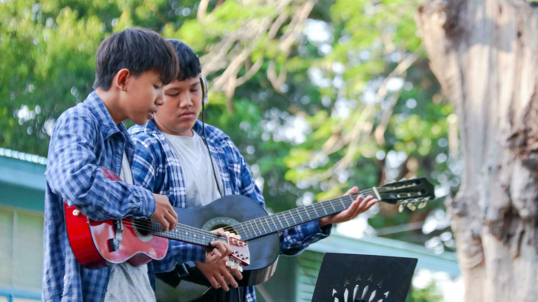 Young Asian boys are playing acoustic guitars in front of a house concept of learning and free time activities photo