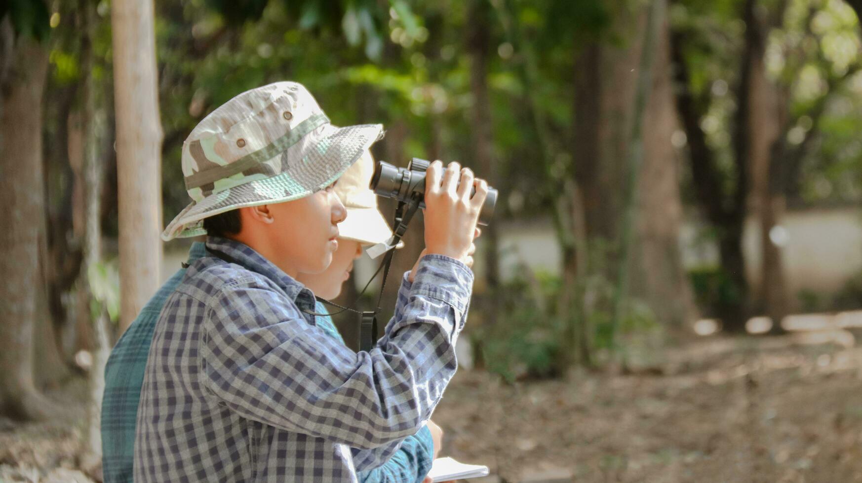 Young Asian boys are using a binocular to lookout for birds and animals in a local park, soft and selective focus photo