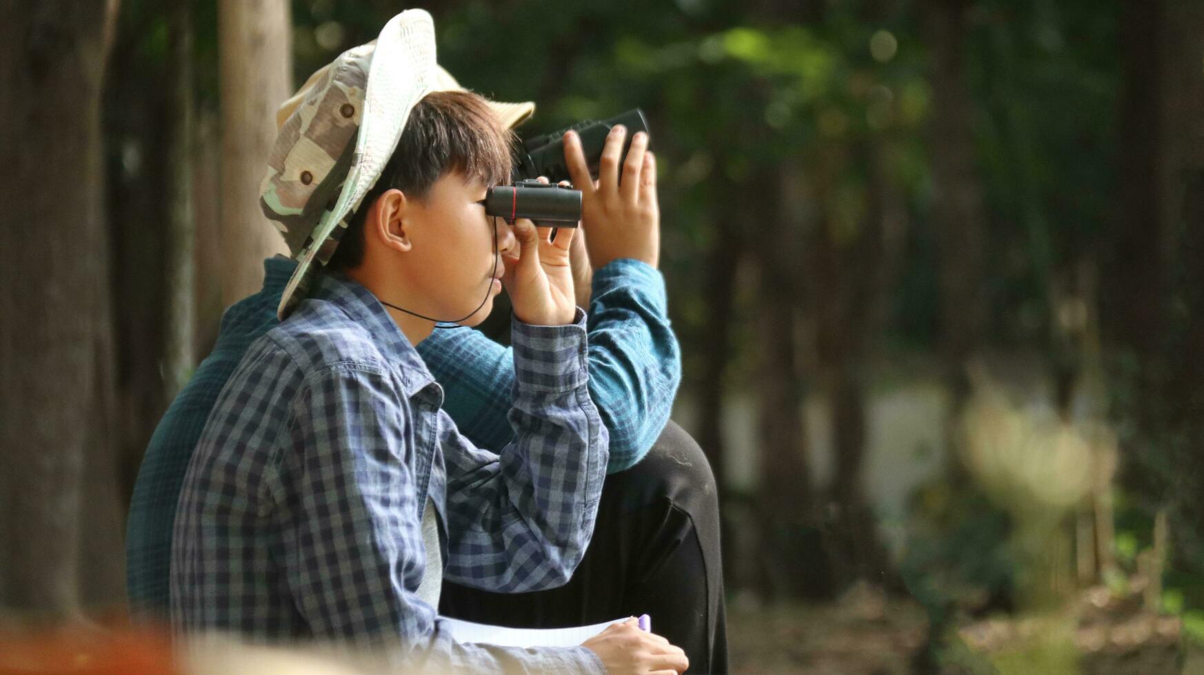 joven asiático Niños son utilizando un binocular a Estar atento para aves y animales en un local parque, suave y selectivo atención foto