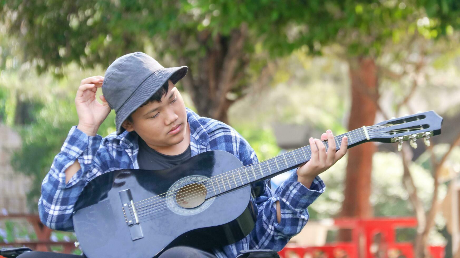 Young Asian boy is playing guitar in a local park, soft and selective focus photo