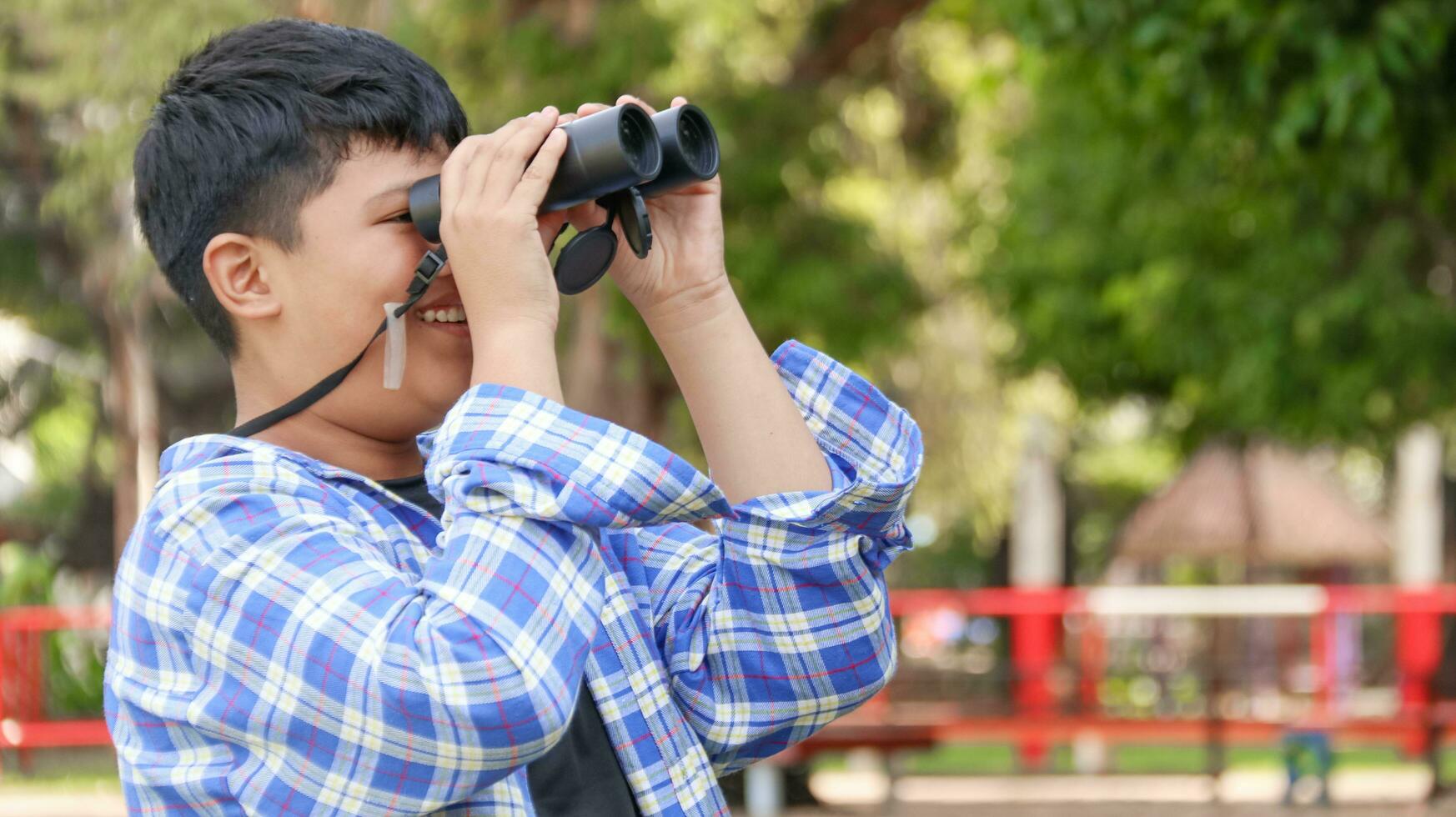 joven asiático chico es utilizando un binocular a Estar atento para aves y animales en un local parque, suave y selectivo atención foto