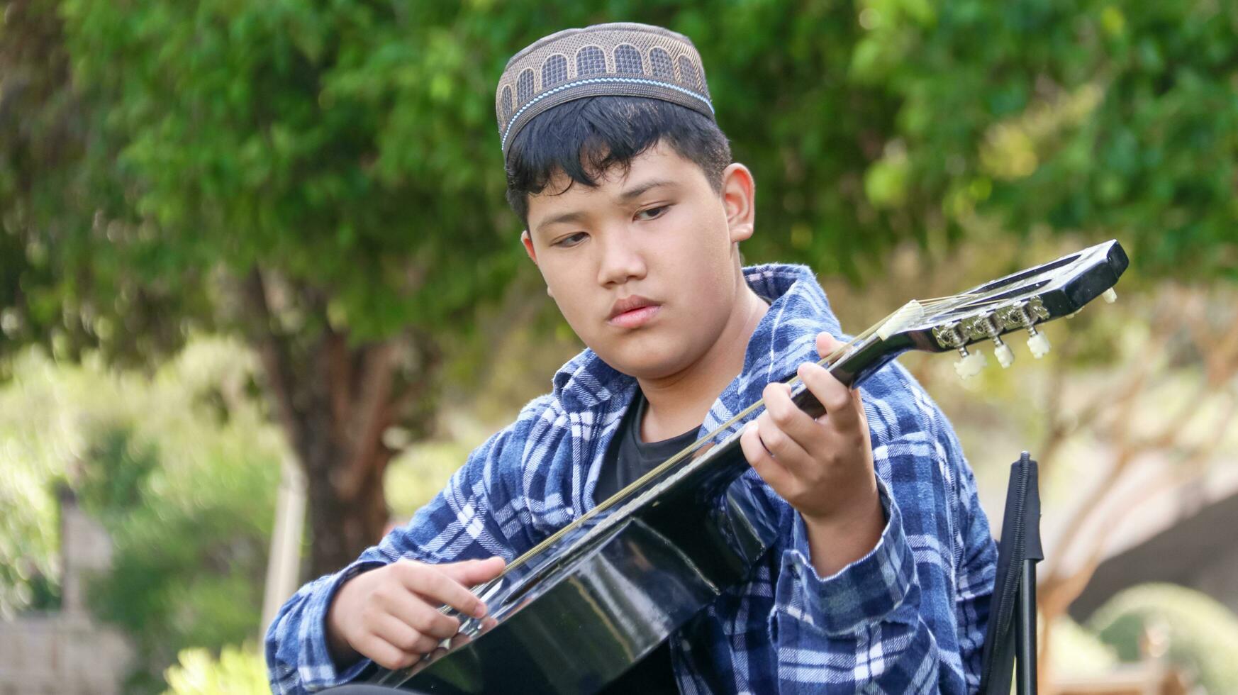 Young Asian boy is playing guitar in a local park, soft and selective focus photo