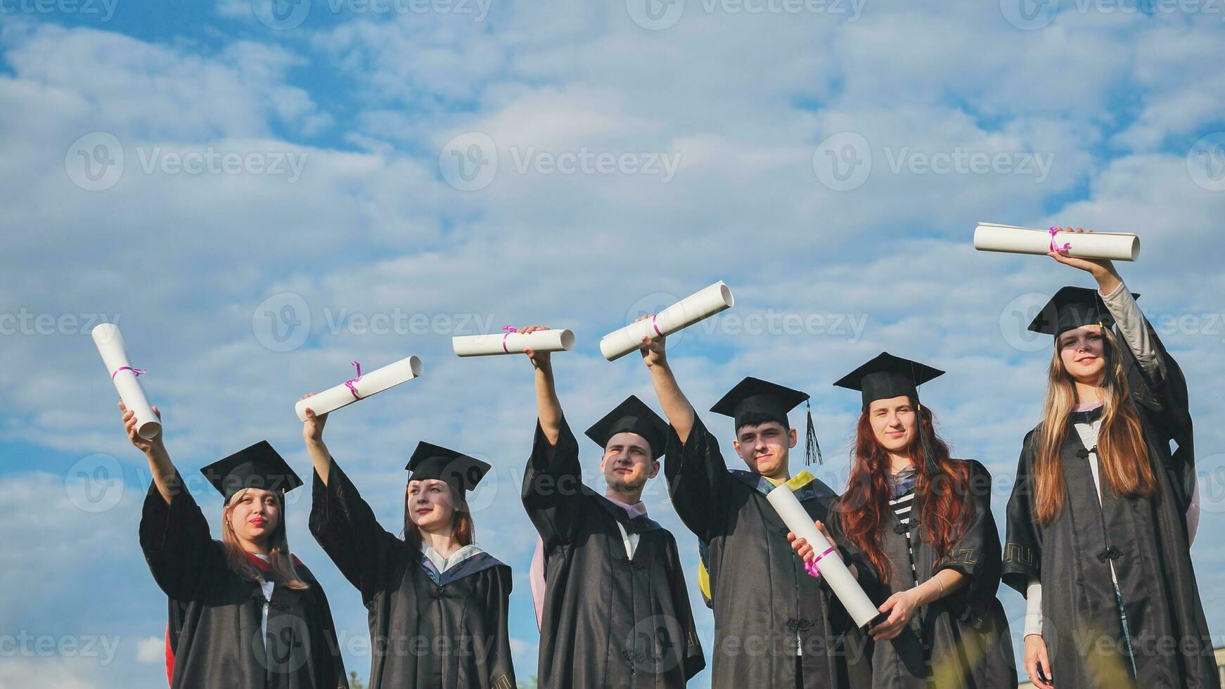 Cheerful graduates pose with raised diplomas on a sunny day. photo