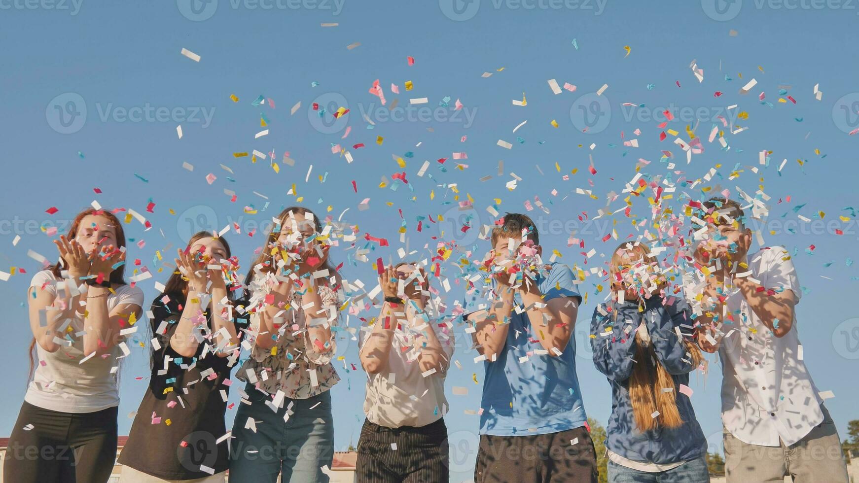 Friends blow colorful paper confetti on a sunny day. photo