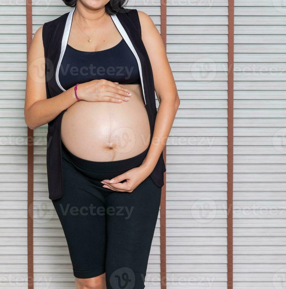 retrato de un embarazada mujer conmovedor su grande barriga cerca arriba, madre, el embarazo, personas y expectativa. mujer participación grande embarazada estómago foto