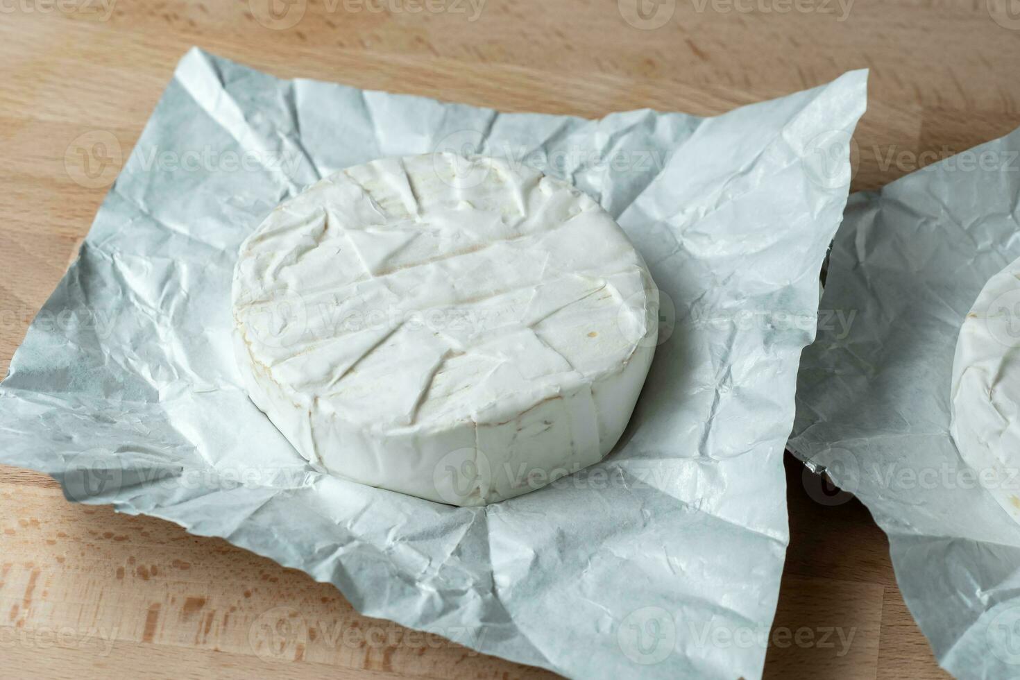 dos cabezas de queso camembert sobre papel blanco en la tabla de cortar. preparación para asar a la parrilla foto