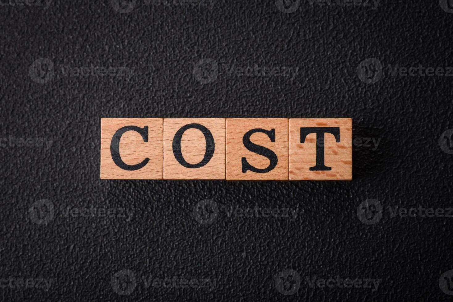 The inscription cost in wooden cubes on a dark concrete background photo