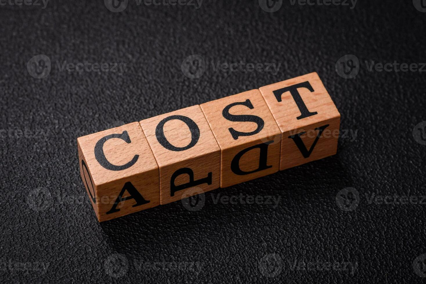 The inscription cost in wooden cubes on a dark concrete background photo