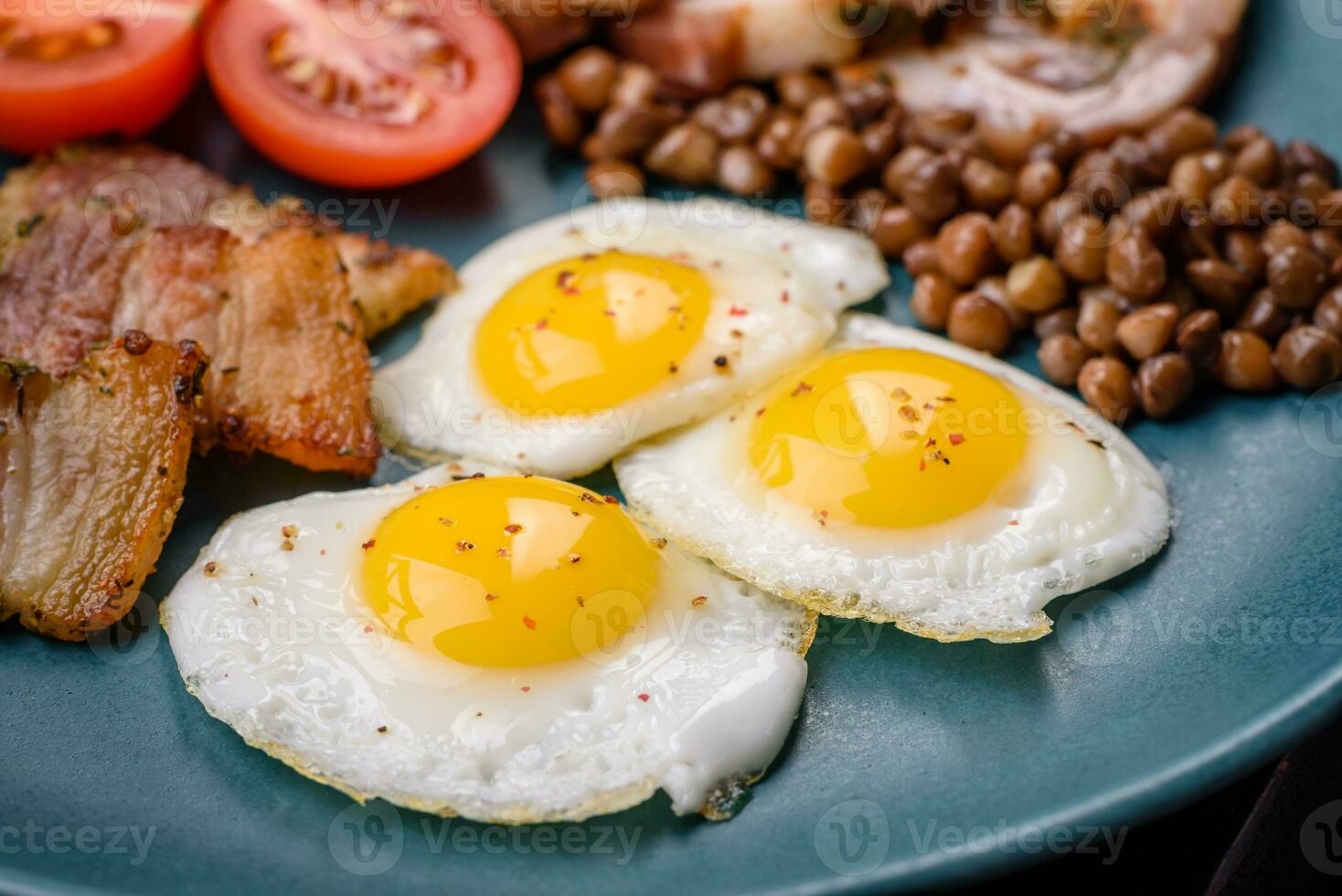 Delicious nutritious breakfast of fried quail eggs, bacon, legumes and cherry tomatoes photo